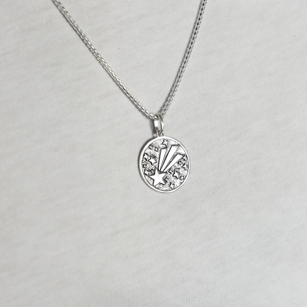 Man wearing a Shooting star pendant in sterling silver on a silver chain with white tshirt background.