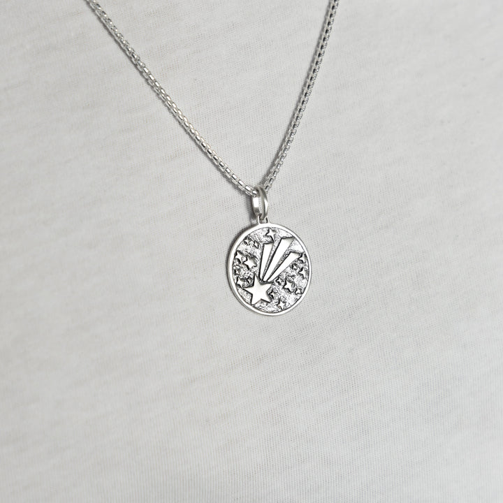 Man wearing a Shooting star pendant in sterling silver on a silver chain with white tshirt background.