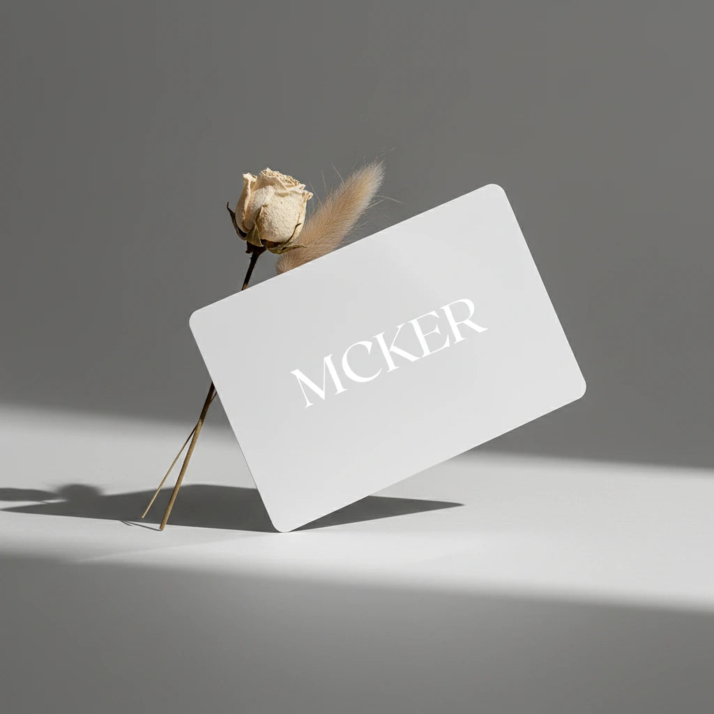 MCKER digital gift card displayed on a minimal grey surface with a dried flower and soft shadow.