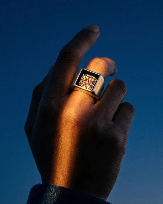 Hand wearing the MCKER Pyramid Ring in sterling silver with a silver textured face under dramatic side lighting.