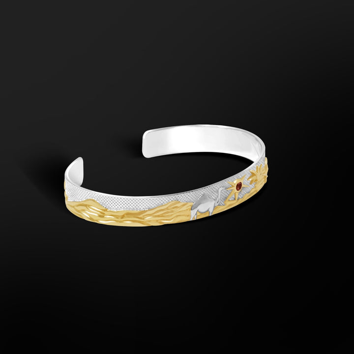 Close-up of the MCKER Sahara Cuff showing raised dunes, palms, camel motif, and 18K gold accents with a 3mm garnet sun